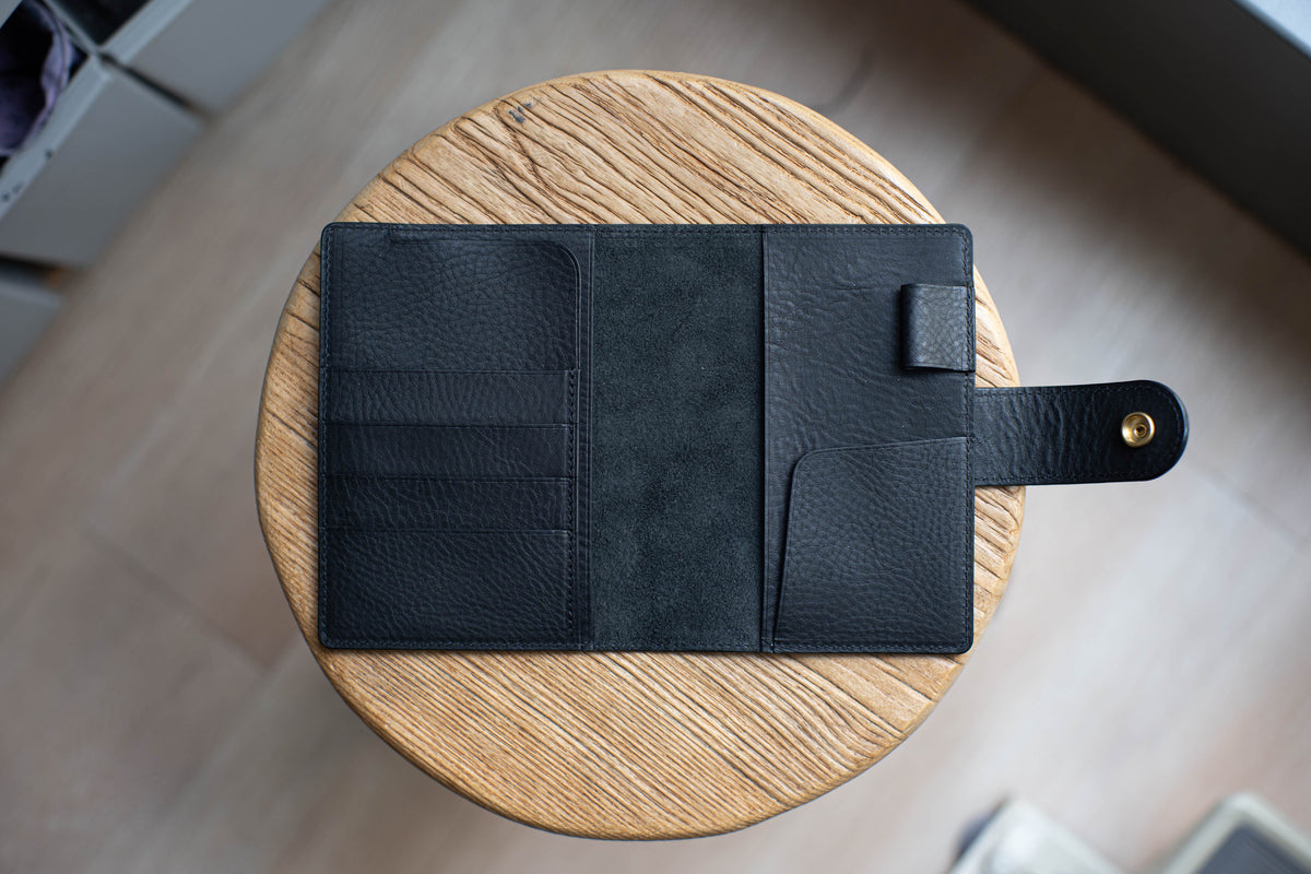 A black leather planner with multiple pockets and a flap closure. The planner is open and lying on a wooden surface.