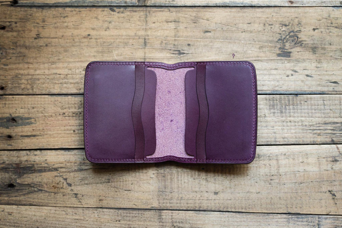 A deep purple leather wallet featuring a bifold design with two interior card slots on each side. The wallet has a smooth exterior finish and a textured, lighter purple suede-like interior lining with visible stitching along the edges.