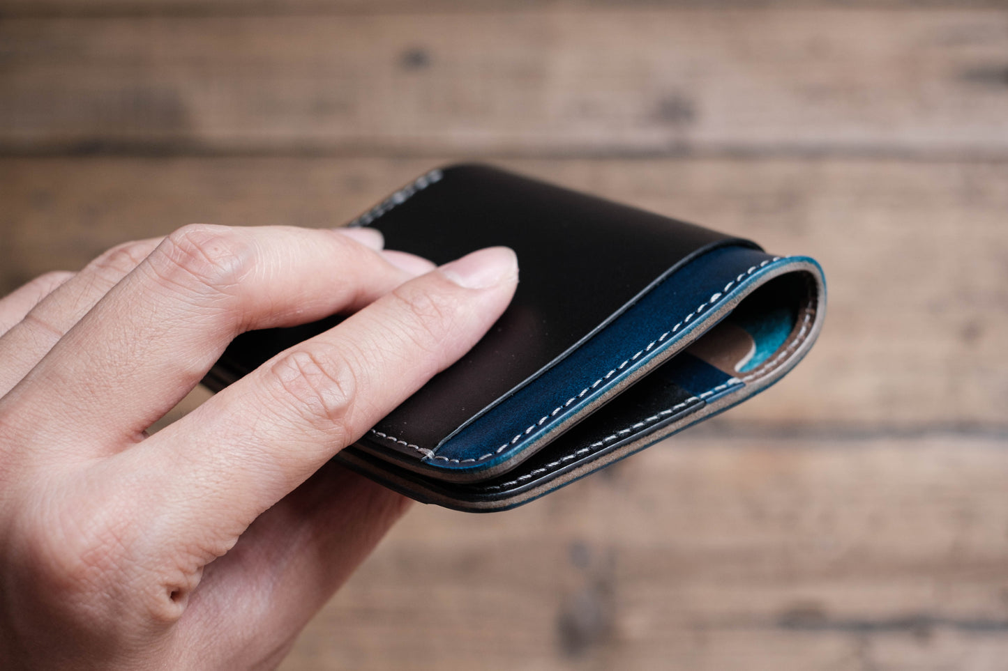 A black leather wallet with a blue stitched edge. The wallet is folded in half and held in a hand.