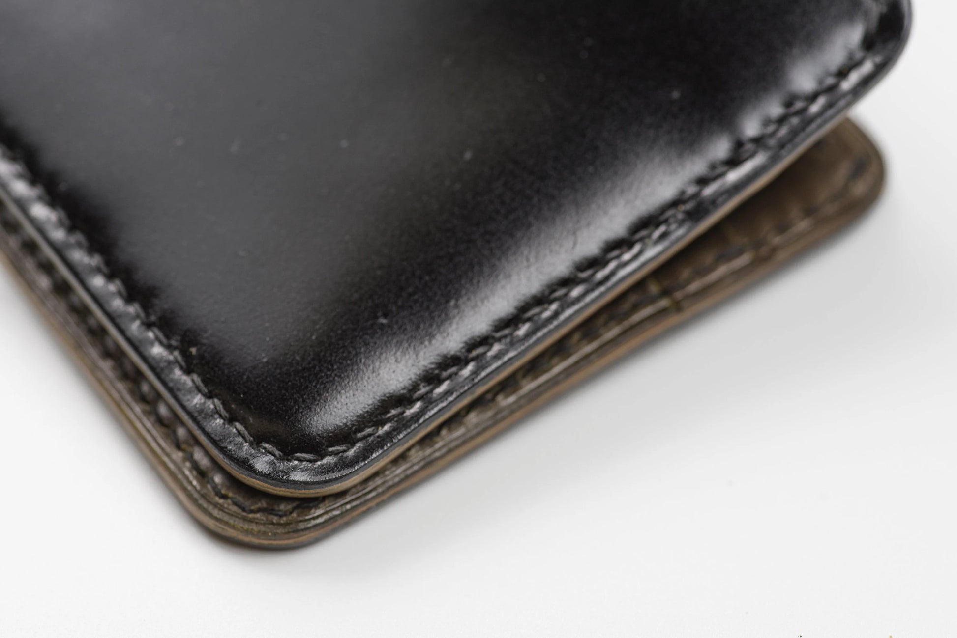 Close-up of a black leather wallet corner showing the smooth exterior, stitched edge, and a olive green interior 