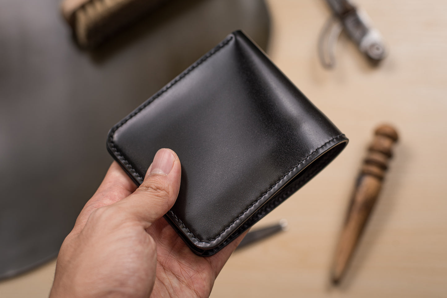 A hand holding a black leather bifold wallet with black stitching