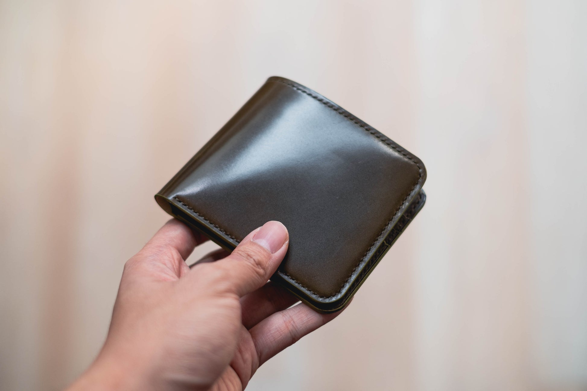 A hand holding a olive green leather bifold wallet 