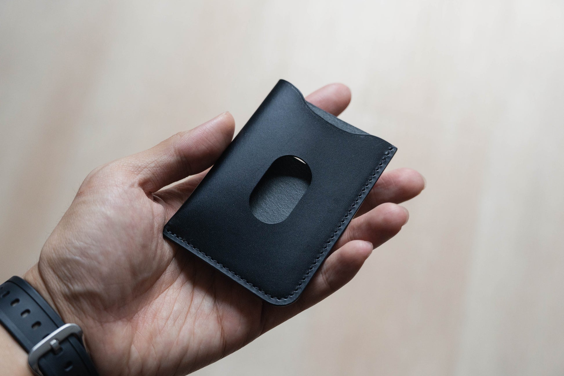 A hand holding a black-colored minimalist card wallet made from Italian Buttero vegetable-tanned leather.