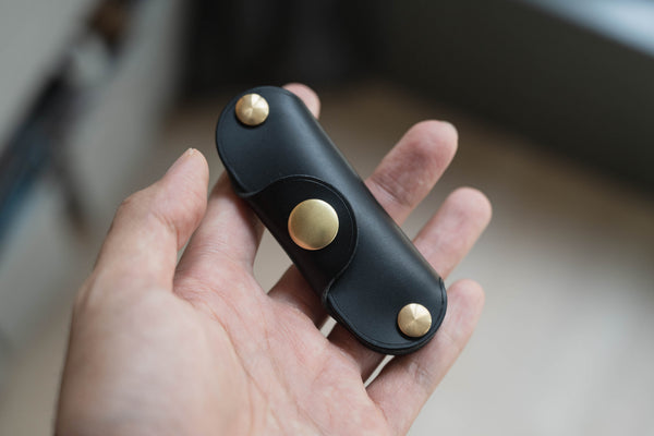 A hand holding a black leather key holder with brass snaps and screws.