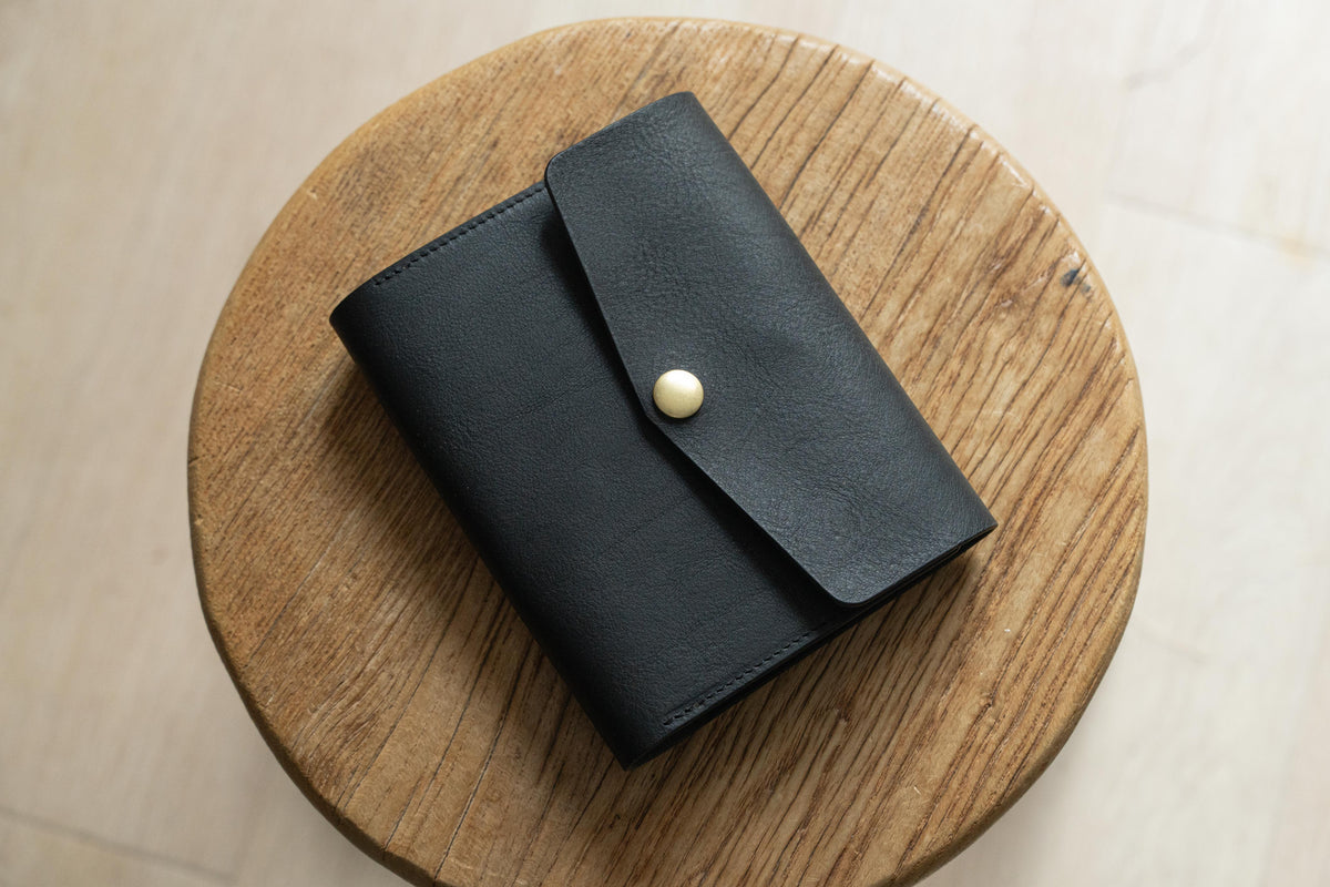 A black leather notebook cover with a flap and a brass button closure.