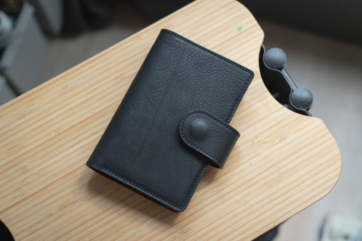A black pebbled leather folio cover with a snap closure and card slots, displayed on a wooden surface.