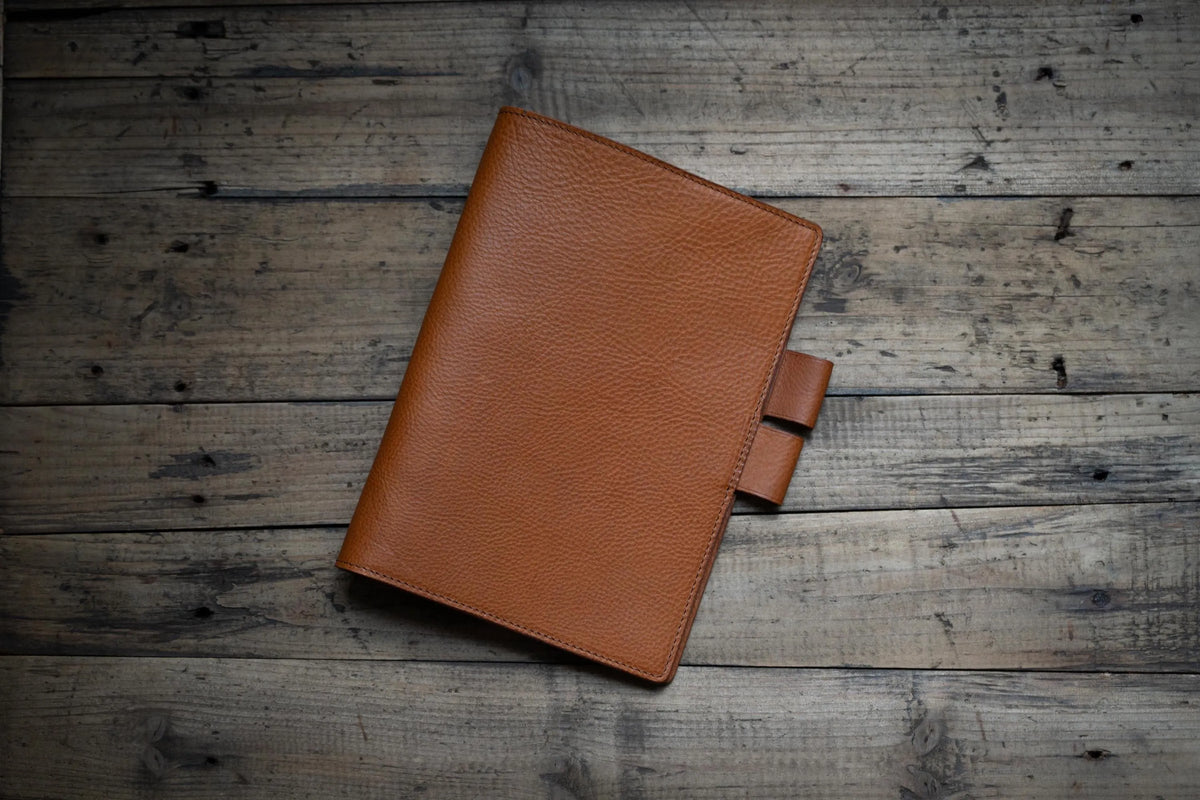 A brown textured leather planner cover with pen loop interlocking closure