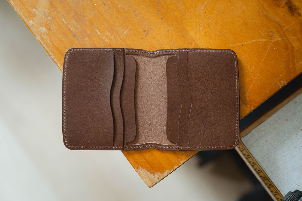 A brown leather bifold wallet featuring four interior card slots with curved edges and a central compartment. The wallet is constructed with visible stitching along the perimeter.