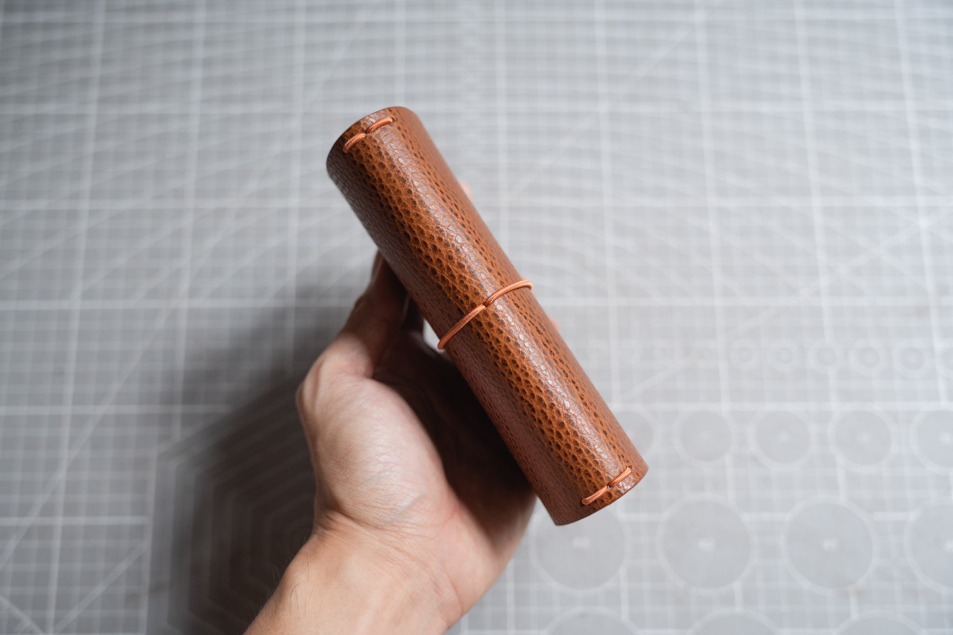 A hand holding a brown textured leather notebook cover - side view -displayed 4 elastic strands 
