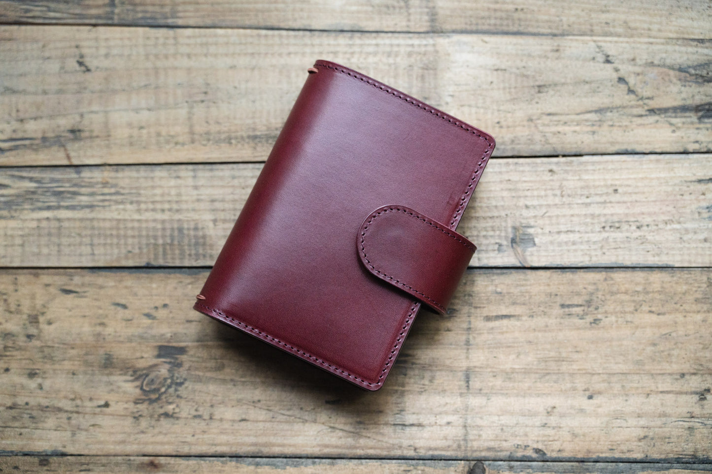 A burgundy Stitched Buttero Leather Traveler's Notebook with Card Slots and elastic strands and pen loop, displayed close