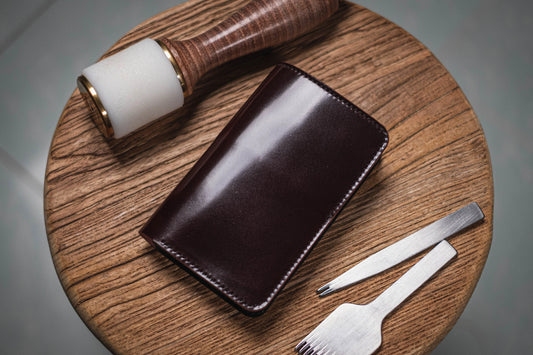 A burgundy shell cordovan middle wallet with a smooth, glossy finish and stitched edges.