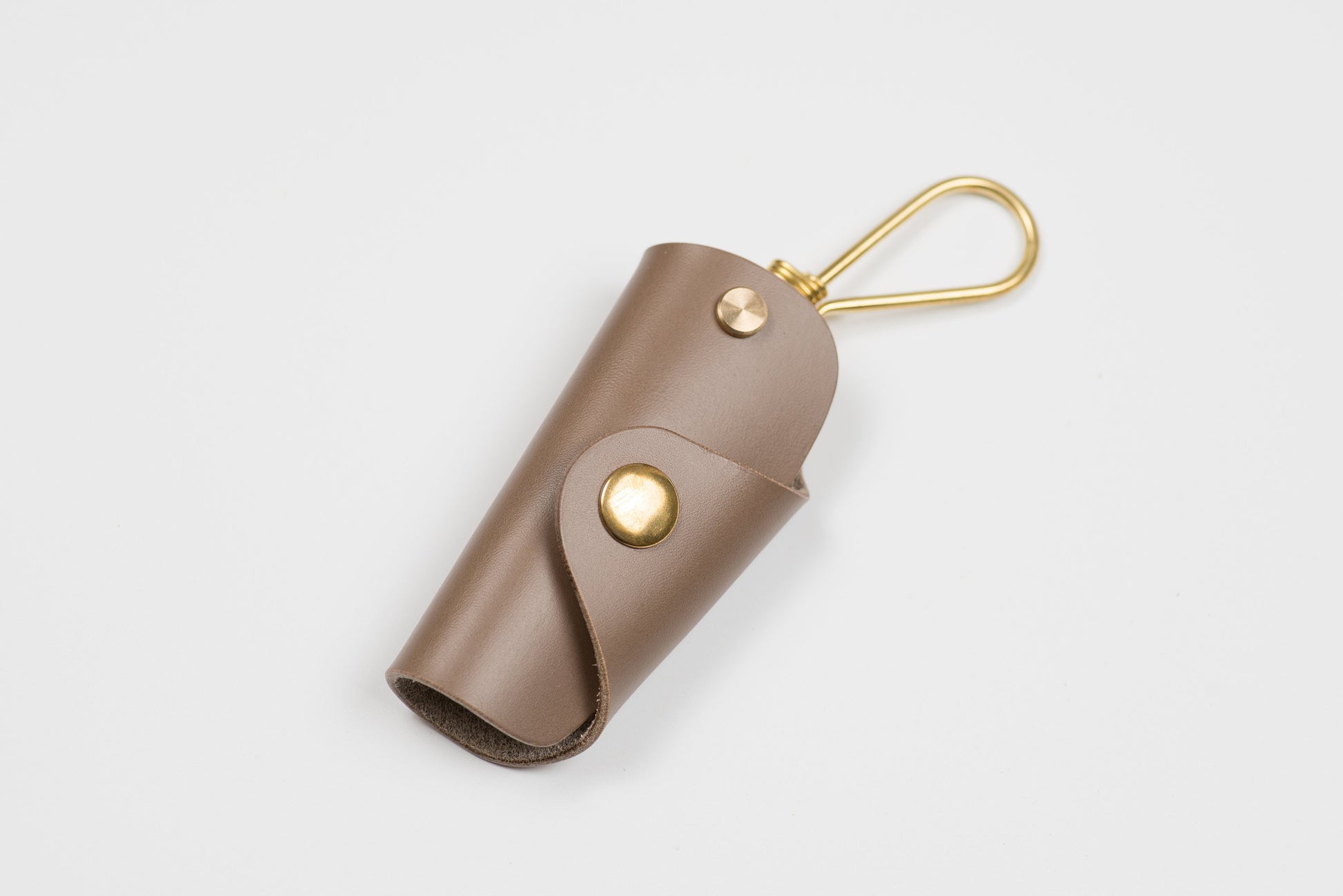 A khaki grey buttero leather key case with brass hardware and a removable brass wire hook.