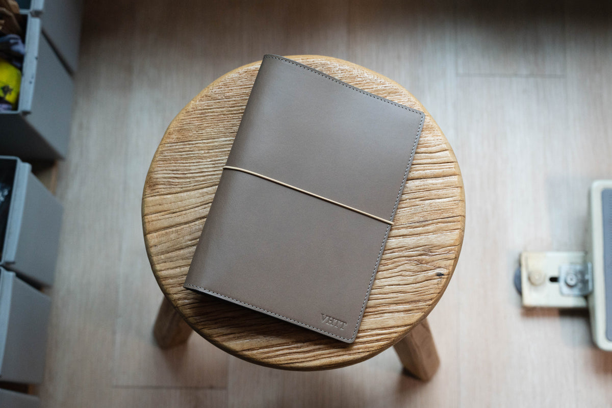 Khaki Grey leather notebook on a round wooden stool with a neutral background