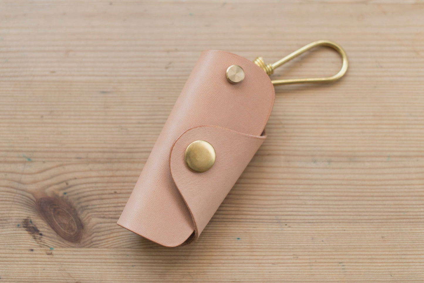 A natural buttero leather key case with brass hardware and a removable brass wire hook.