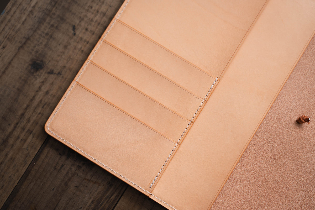 A natural leather notebook cover with multiple card slots and a stitched edge.