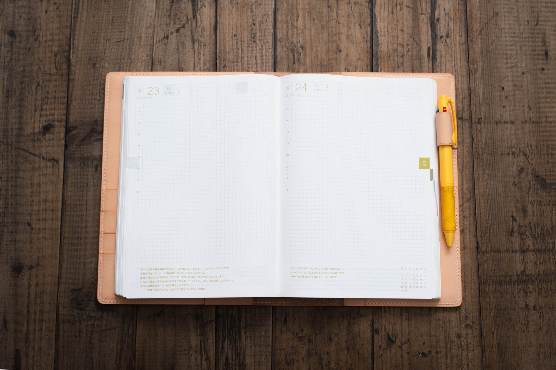 An open, blank, cream-colored, leather-bound planner with a yellow pen tucked into the right side binding. 