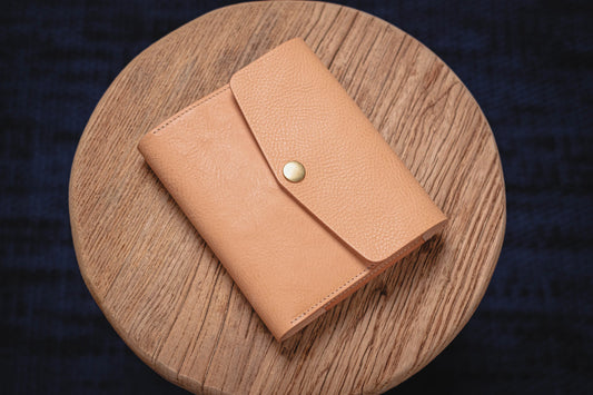 A natural leather notebook cover with a flap and a brass button closure.