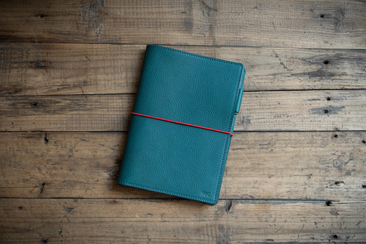 A navy blue pebbled leather notebook cover with an red elastic band closure
