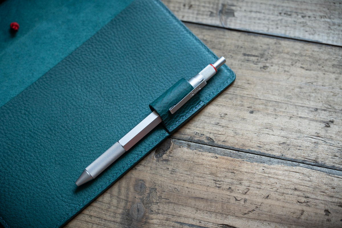 Close-up of the pen loop of a navy blue leather notebook. A sliver pen insert into the pen loop attached on the leather cover.