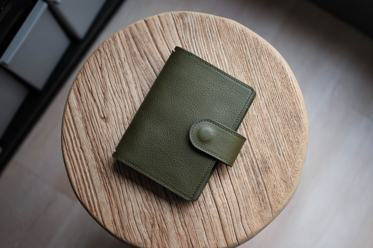 A olive green pebbled leather traveler's notebook with a strap closure, displayed closed