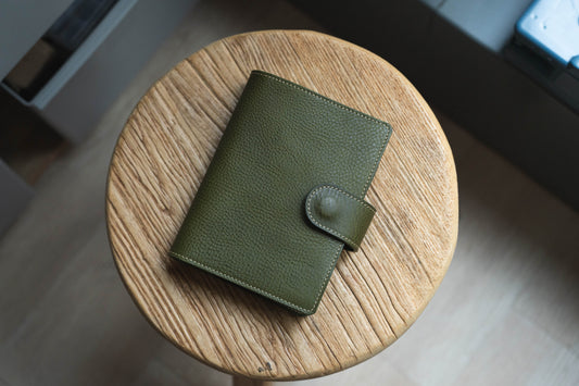 A olive green pebbled leather notebook cover with brass snaps, designed for an A6+ size notebook.