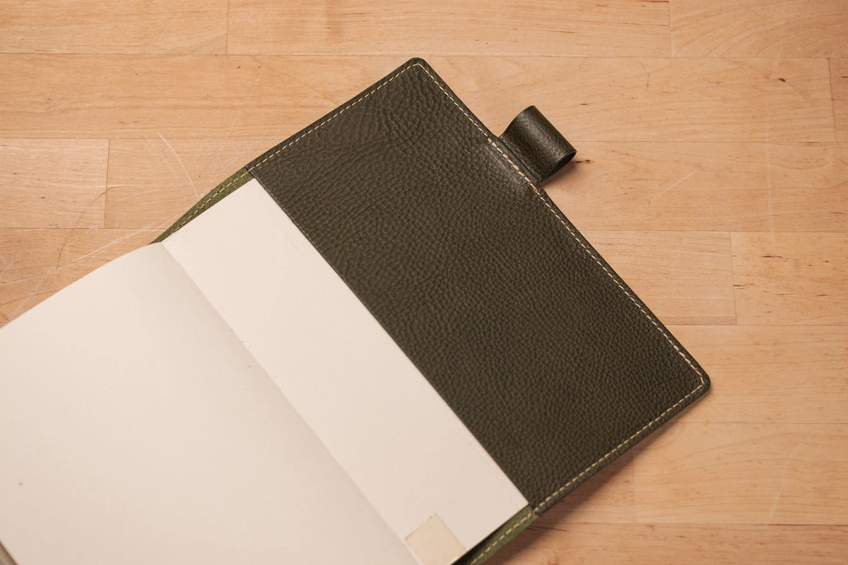 A green leather notebook cover with a flap and a pen loop. The cover is opened and the inside of the notebook is visible.
