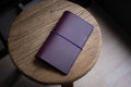 A purple Stitched Buttero Leather Traveler's Notebook and a elastic enclouse, displayed close