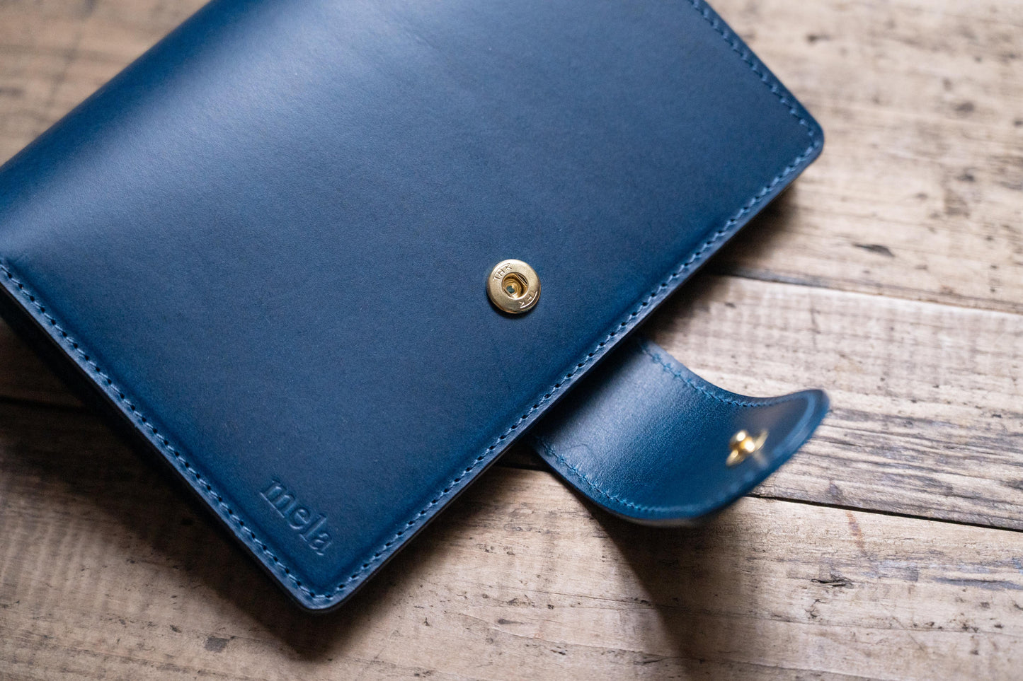 A navy blue Stitched Buttero Leather Traveler's Notebook with Card Slots, displayed close, close up of a leather strap and stitching and solid brass button