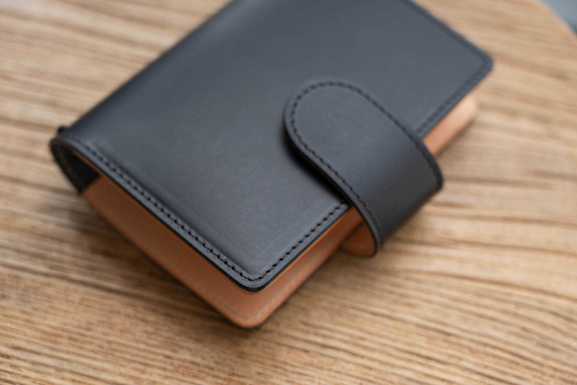 A black and natural two-tone leather traveler's notebook with card slots, displayed closed, close up of stitching and snap closure