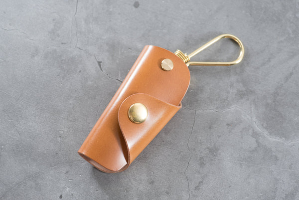 A whiskey Shell Cordovan leather key case with brass hardware and a removable brass wire hook.