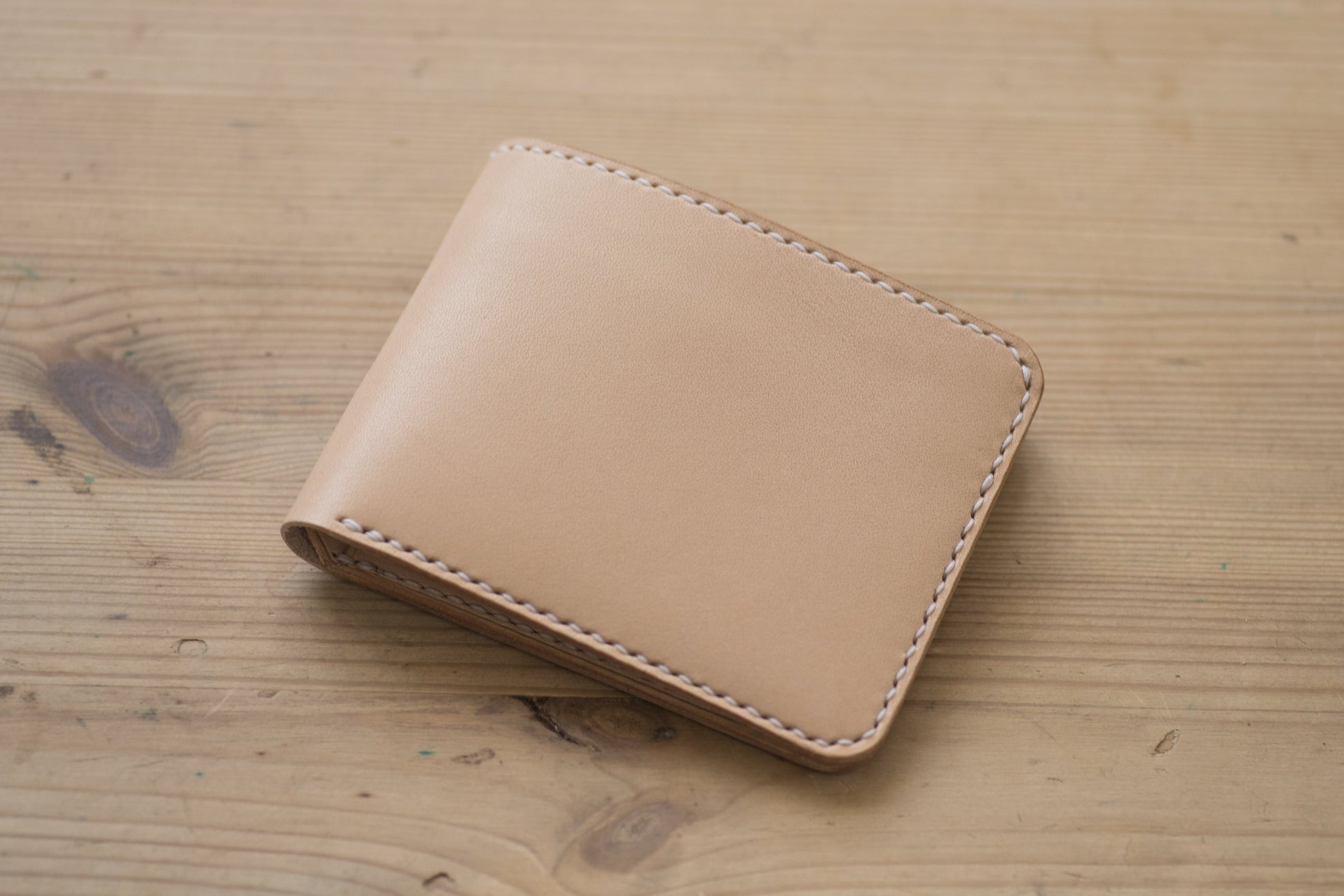 A natural leather wallet with white stitching around the edges.