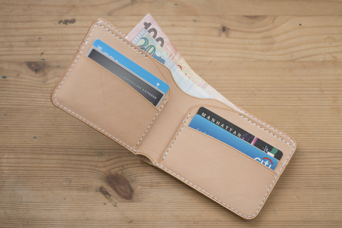 A natural leather wallet with white stitching, open to reveal 4 credit cards and cash. 