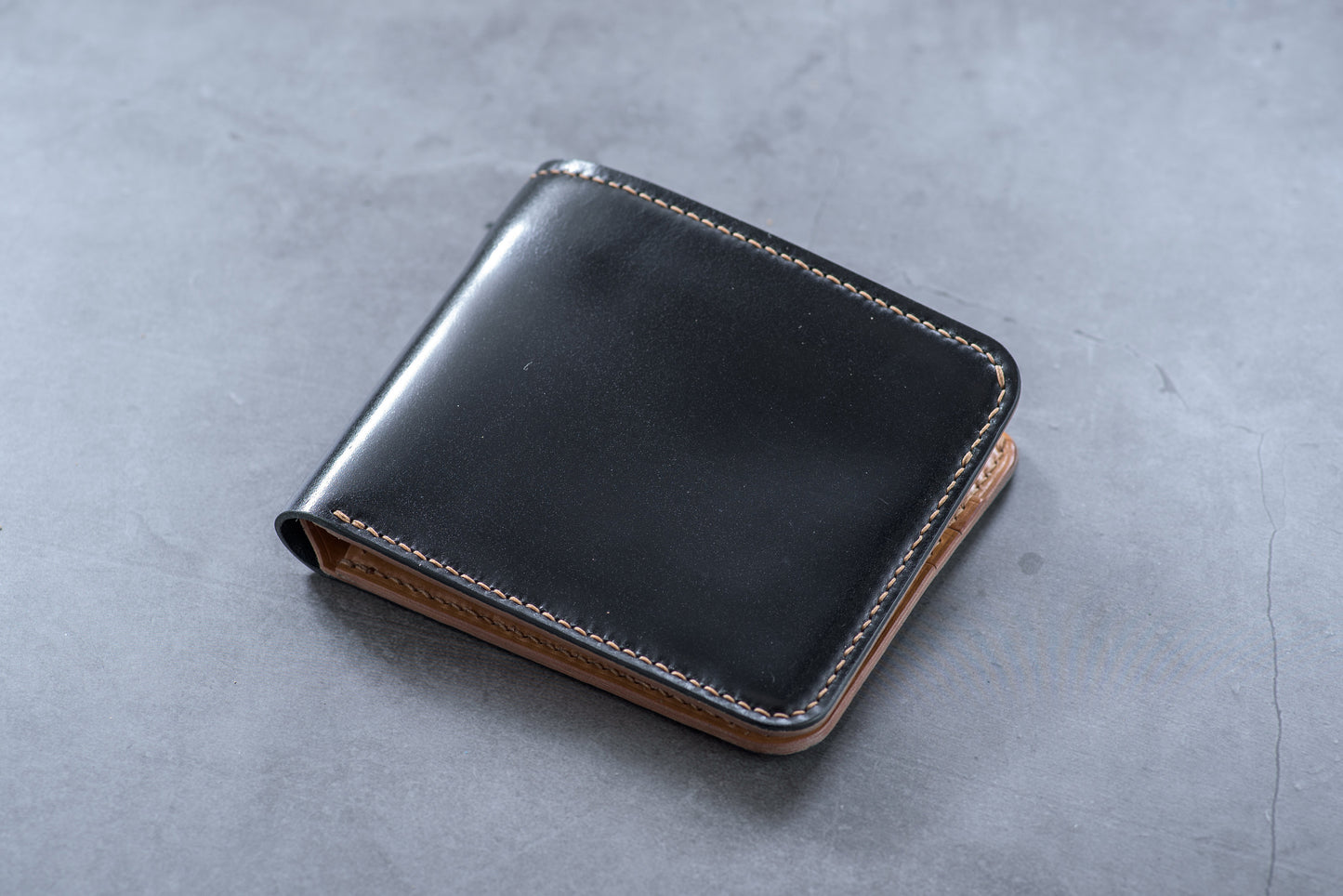 A closed black and whiskey shell cordovan leather billfold wallet with visible hand-saddle stitching.