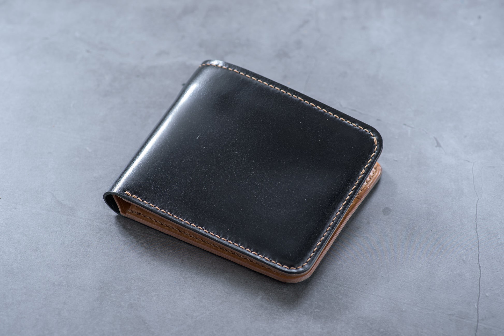 A closed black and whiskey shell cordovan leather billfold wallet with visible hand-saddle stitching.