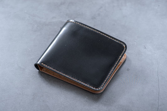 A closed black and whiskey shell cordovan leather billfold wallet with visible hand-saddle stitching.