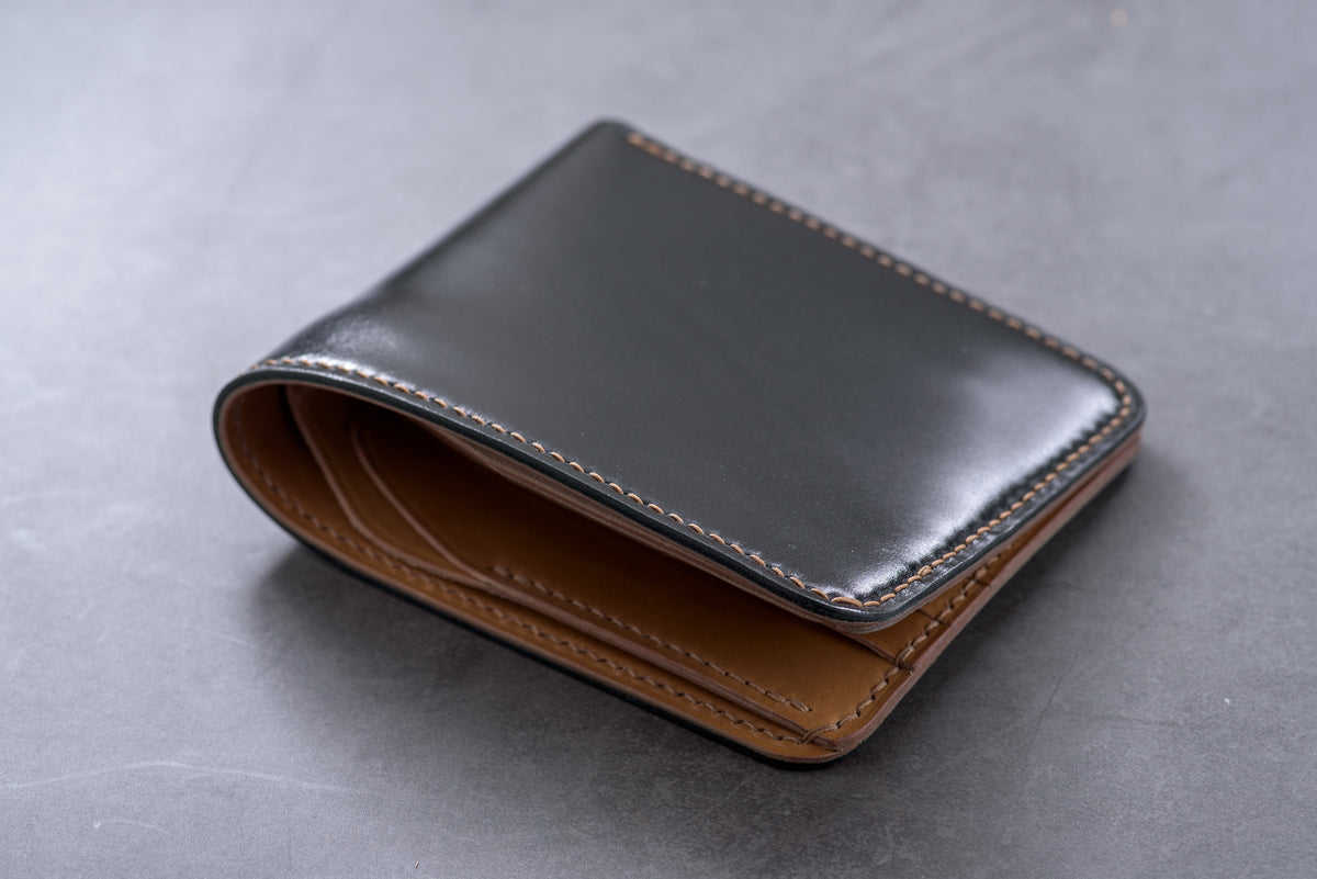 A black leather wallet with a whiskey leather interior and a stitched edge.