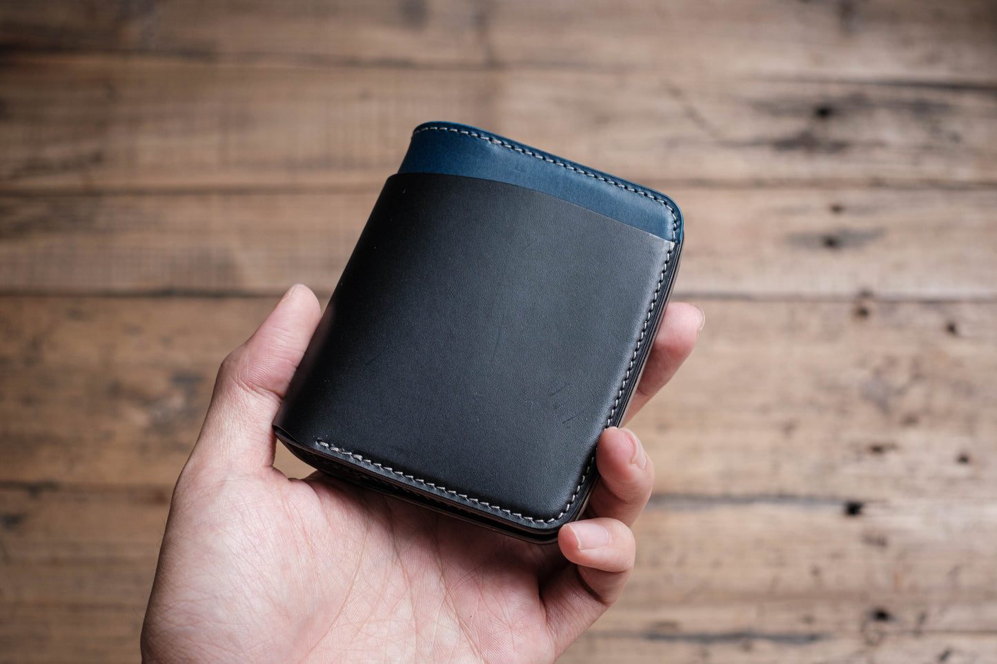 A hand holding a folded wallet with black, navy, and grey colors, made of Buttero Vegetable Tanned Leather.