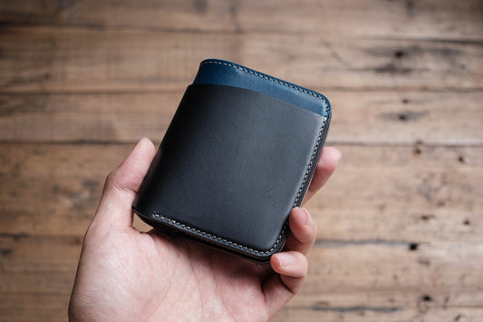 A hand holding a folded wallet with black, navy, and grey colors, made of Buttero Vegetable Tanned Leather.