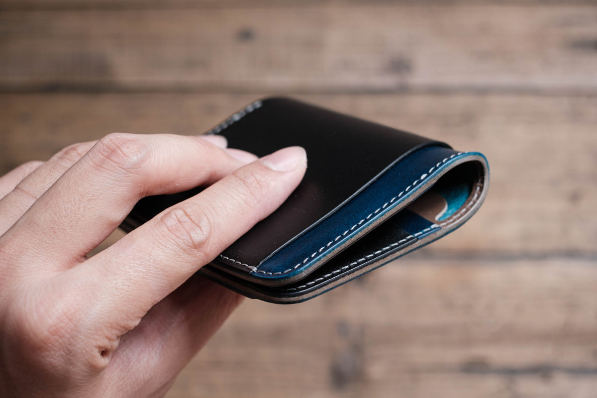 A black leather wallet with a blue stitched edge. The wallet is folded in half and held in a hand.