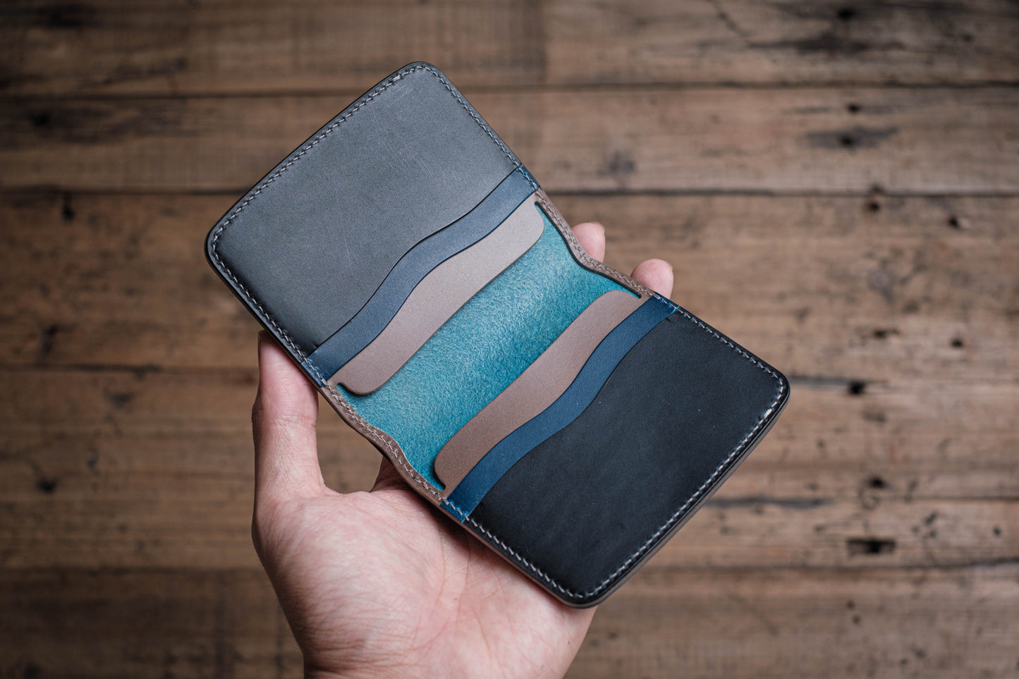 A blue leather wallet with multiple card slots, open to reveal the interior lining in shades of blue, black, and gray.