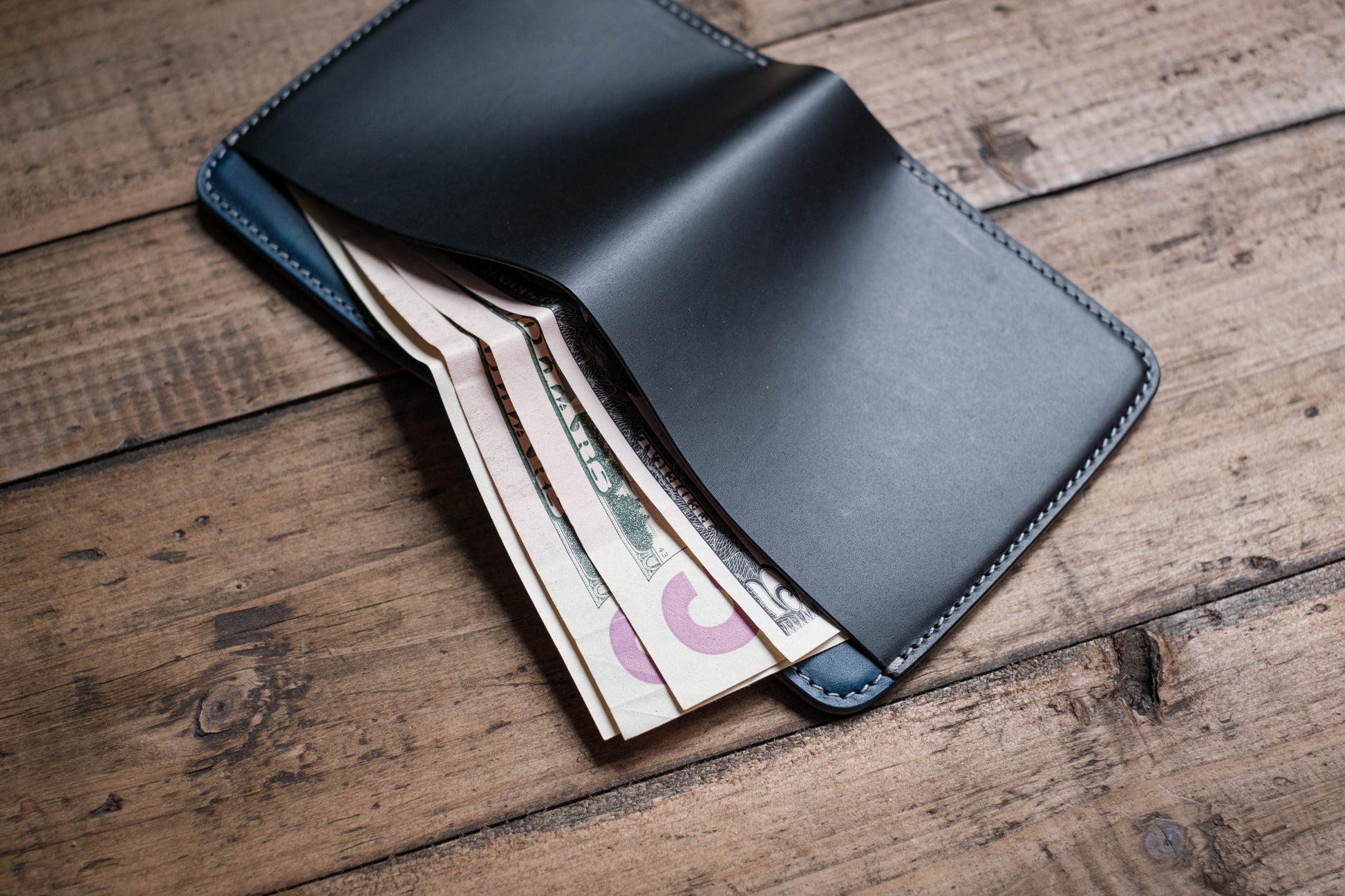 A black leather wallet with a blue interior, open to reveal several bills of US currency.