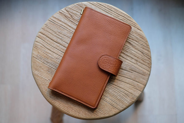 A brown lined traveler's notebook with card slots and a leather strap, displayed close