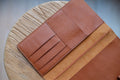 A brown leather traveler's notebook with card slots and a snap button closure, displayed open, close up of left card slots
