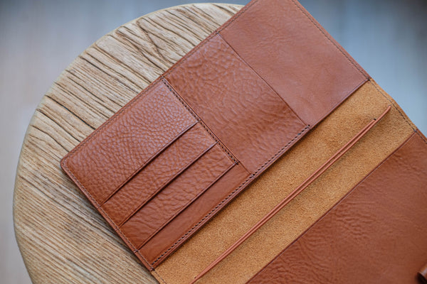 A brown leather traveler's notebook with card slots and a snap button closure, displayed open, close up of left card slots
