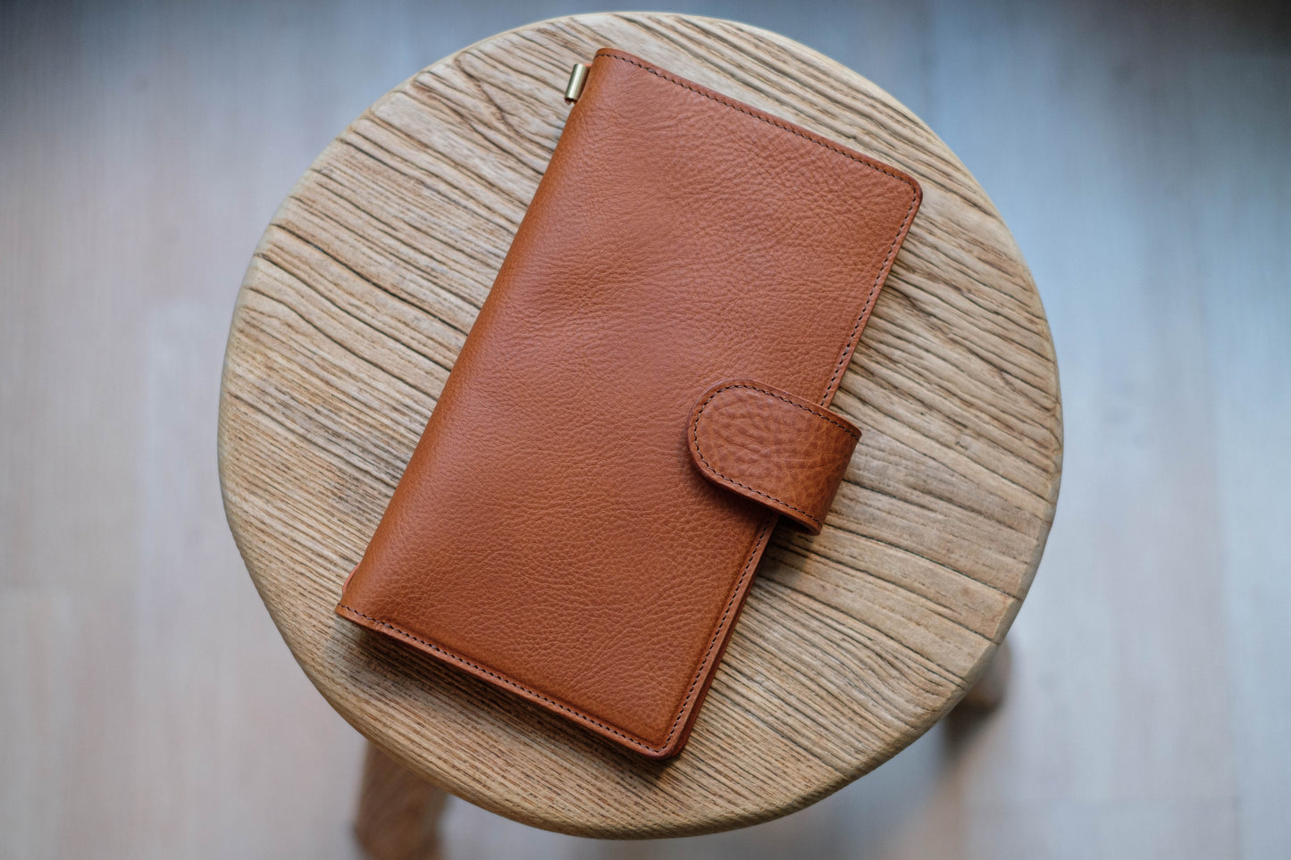 A brown leather traveler's notebook with card slots and a snap button closure, displayed closed