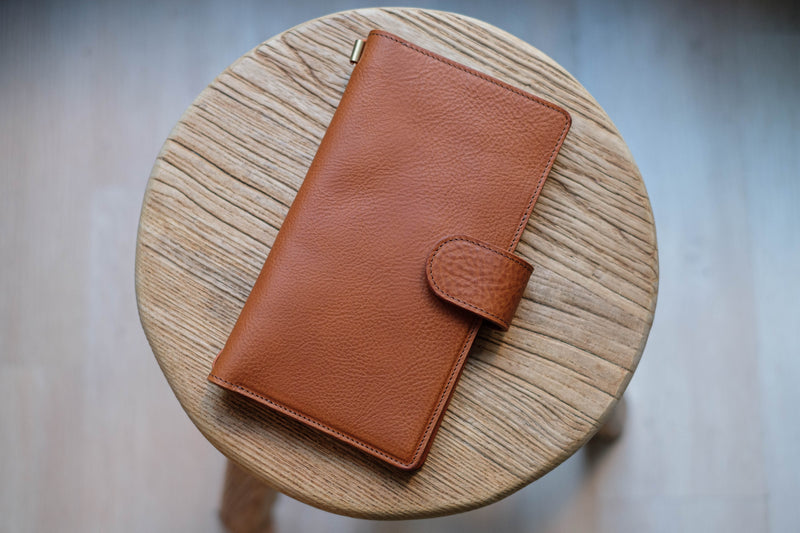 A brown leather traveler's notebook with card slots and a snap button closure, displayed closed