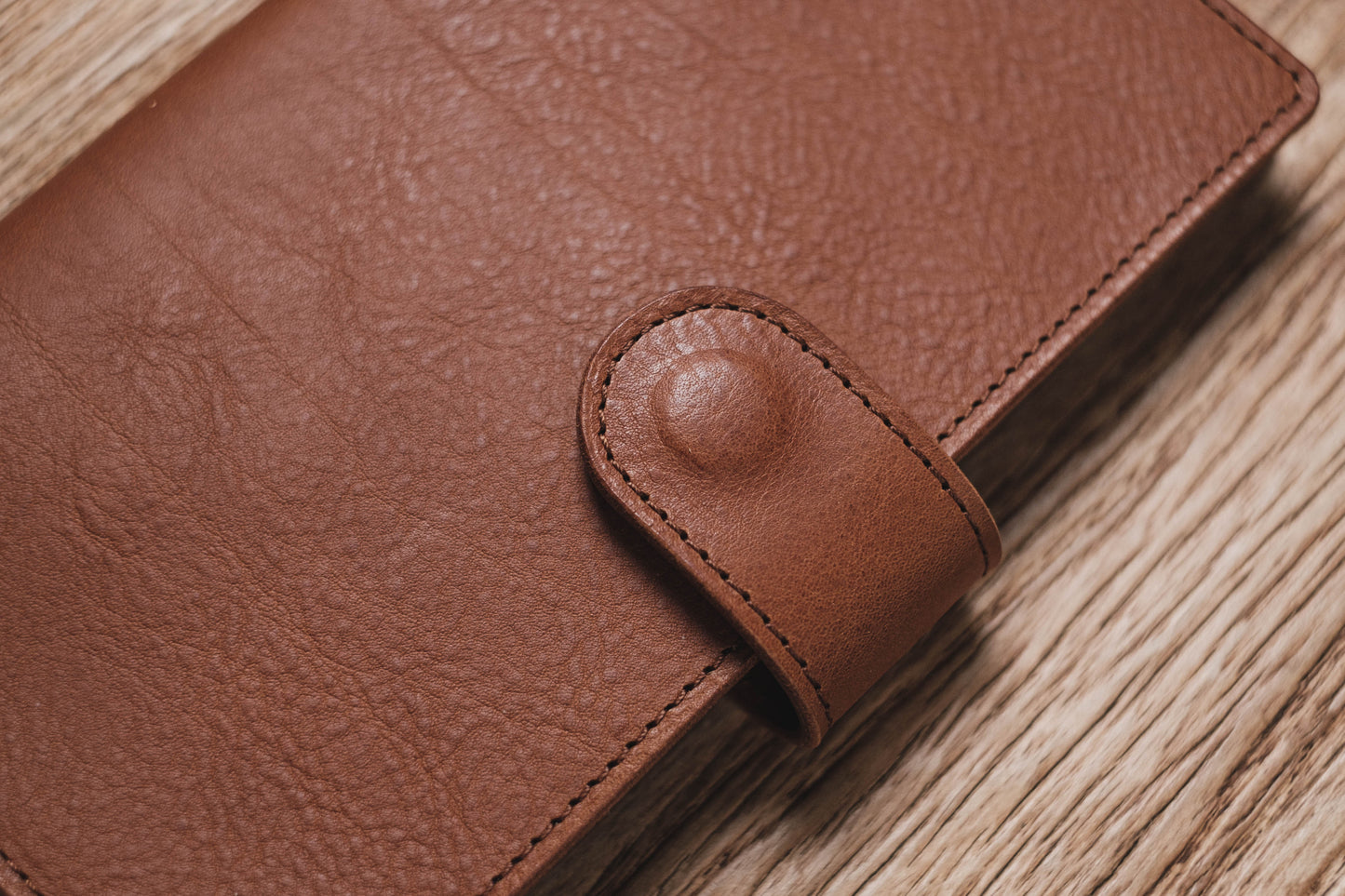 A brown pebbled leather traveler's notebook with a strap closure, displayed closed, close up of snap closure and stitching