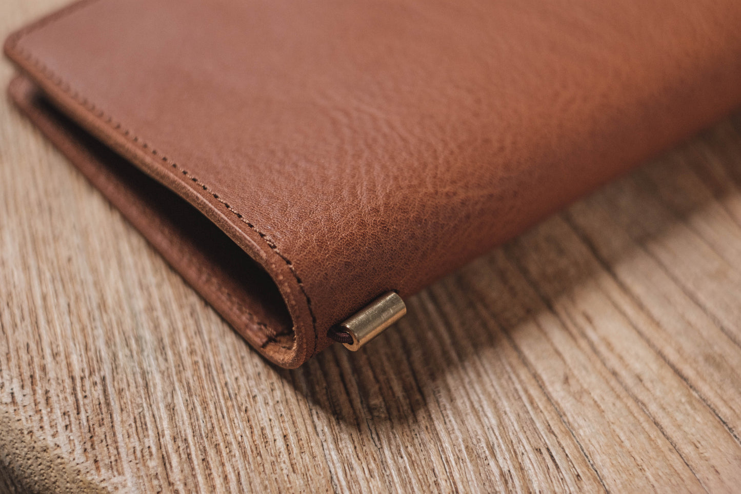 A brown pebbled leather traveler's notebook with a strap closure, displayed closed, close up of stitching and elastic strands