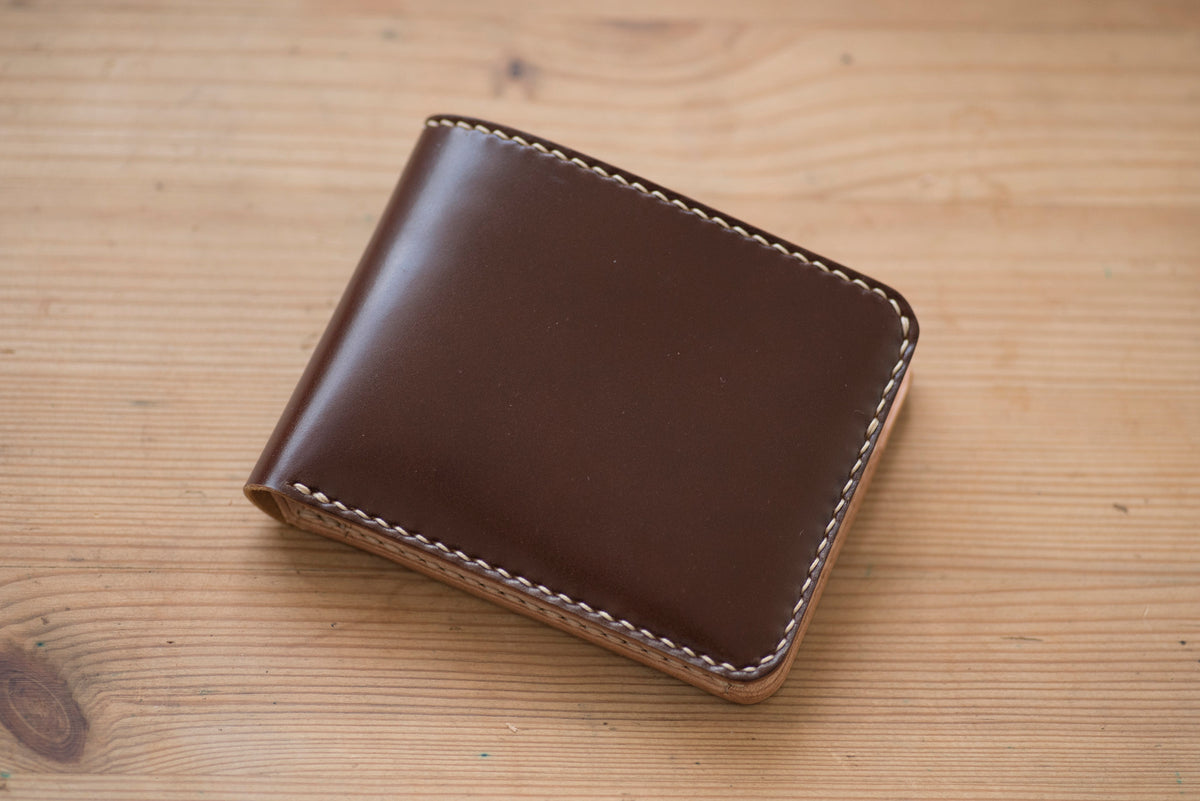 A brown shell cordovan and natural two-tone billfold wallet with visible stitching and a coin pocket