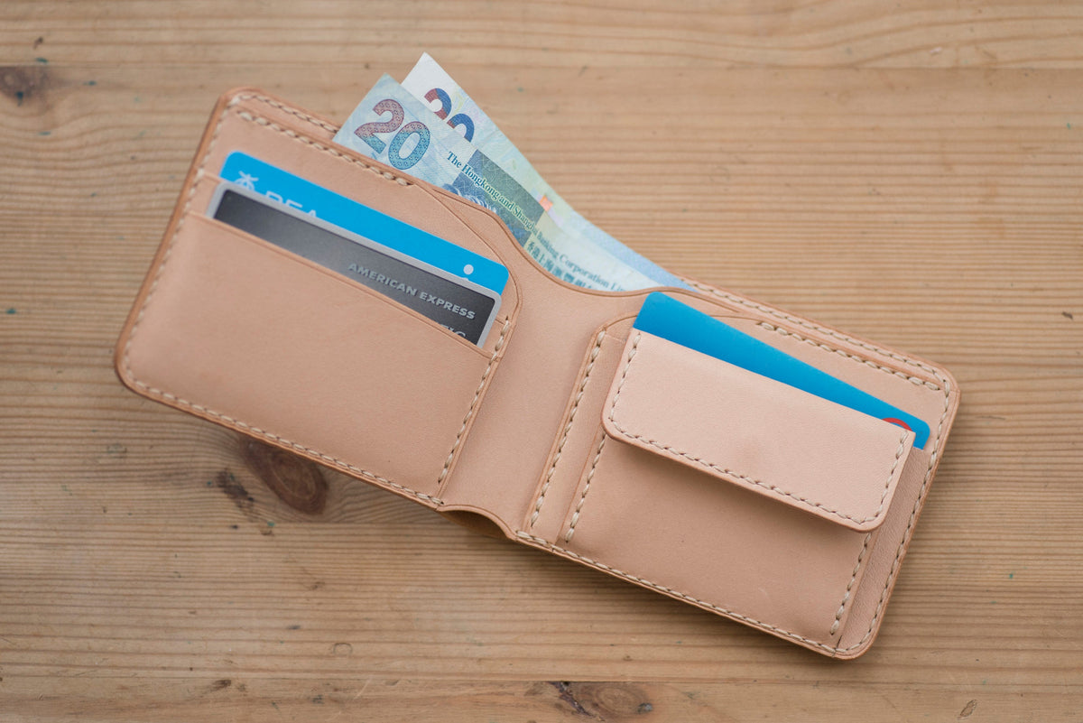 A natural leather wallet with a stitched edge is open, revealing 2 cards, and two bills.